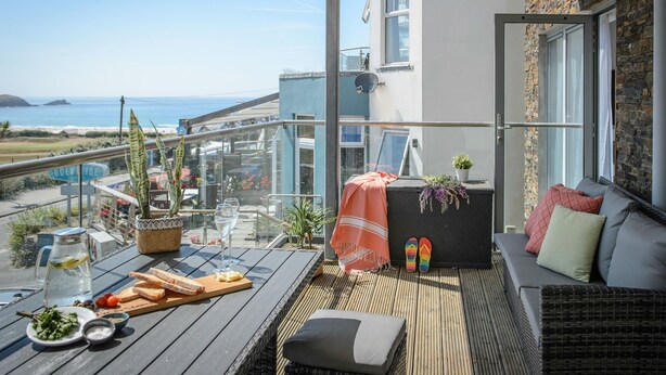 Een balkon met uitzicht op de oceaan, een tafel met eten en drinken, en een zithoek met kussens.