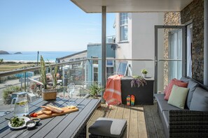Ein Balkon mit Meerblick, ein Tisch mit Speisen und Getränken sowie eine Sitzecke mit Kissen.