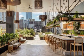 Enjoy a drink at the rooftop bar with a city view, surrounded by lush plants and comfortable seating areas.
