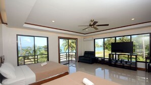 A spacious room with two beds, a sofa, a TV, and large windows offering a view of palm trees and the sea. - El Nido Palms Resort (El Nido)