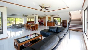A spacious living area with a large sofa, a glass coffee table, and a dining table. There is a kitchen in the background and a staircase leading to another level. - El Nido Palms Resort (El Nido)