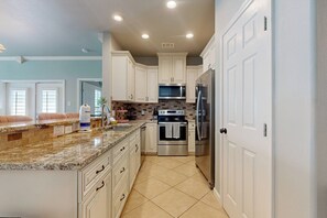 A modern kitchen with white cabinets, a granite countertop, stainless steel appliances, and a tiled floor. - Shared Pool, Golf Cart Access (Port Aransas)