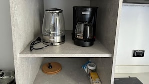 Una cocina con cafetera y jarra de vidrio en una estantería.