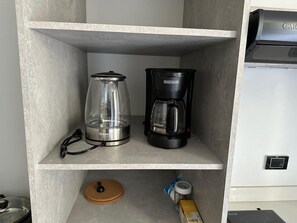 Eine Küchenzeile mit einer Kaffeemaschine und einer Glaskaraffe auf einem Regal.