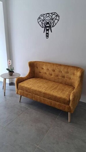 Ein senfgelbes Sofa vor einer weißen Wand, darüber ein geometrisches Wandkunstwerk.