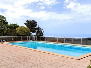A rectangular swimming pool with a clear blue water surface, surrounded by a tiled deck and a glass railing.