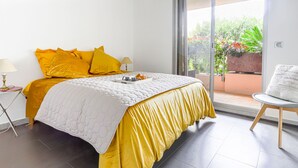 A bedroom with a bed, a chair, a nightstand, and a view of the outdoors through a sliding door. - Les Balcons d'Eze by Interhome (Eze)