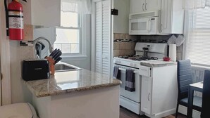 Una cocina compacta con gabinetes blancos, cocina a gas, microondas y tostadora.