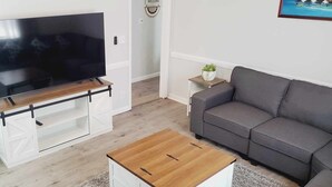 Una sala de estar con televisor de pantalla plana sobre un mueble de madera, un sofá gris y una mesa de centro de madera.