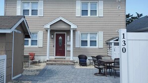 Una casa de dos pisos con puerta frontal roja, contraventanas blancas y un camino de ladrillo que conduce a un patio con mobiliario exterior.