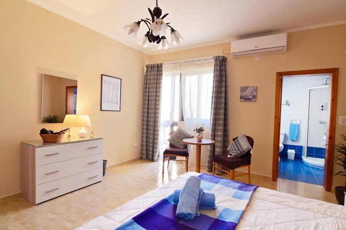 A hotel room with a bed, a desk, a chair, a lamp, a dresser, and a bathroom visible through an open door.