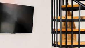 A modern living room with a white sofa, a flat-screen TV mounted on the wall, and a wooden staircase. - The Jungalows (Lunukalapuwa)