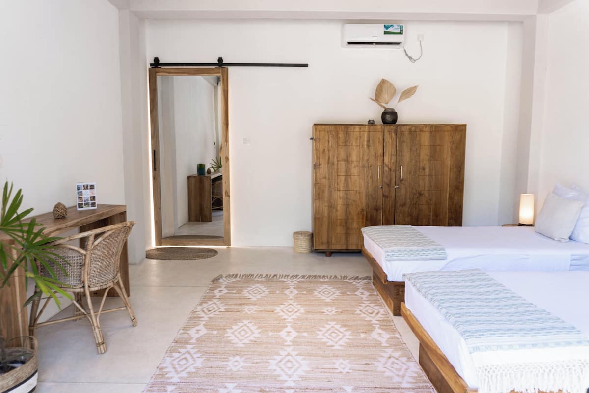 A bedroom with a bed, a wooden wardrobe, a desk with a chair, and a patterned rug.
