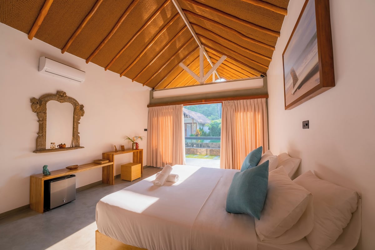 A bedroom with a large bed, a wooden desk, a mirror, and a window with curtains.