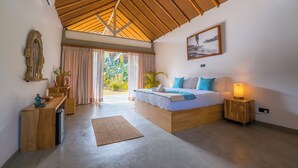 A bedroom with a wooden ceiling, a bed with pillows, a bedside lamp, a small wooden cabinet, and a large window with curtains. - The Jungalows (Lunukalapuwa)