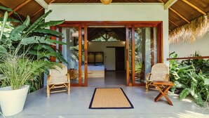 A covered outdoor area with two wicker chairs, a large potted plant, and a mat on the floor. - The Jungalows (Lunukalapuwa)