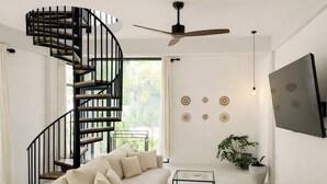 A modern living room with a spiral staircase, a sofa, a coffee table, a TV, and decorative wall art. - The Jungalows (Lunukalapuwa)