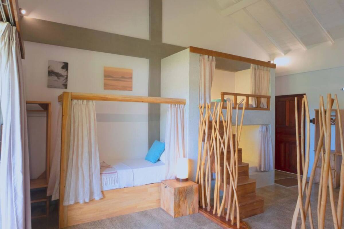 A room with a wooden bunk bed, a small seating area with a cushion, and a staircase with wooden railings.
