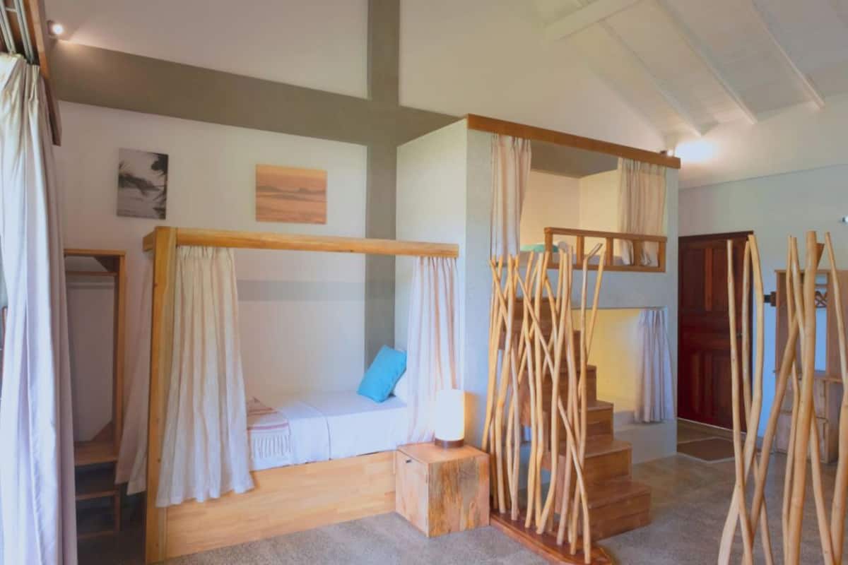 Ein Zimmer mit einem Holzbett, einer kleinen Sitzecke mit Kissen und einer Treppe mit Holzhandläufen.
