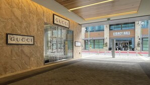 Eine moderne Gebäudefassade mit den Schildern 'GUCCI' und 'LEGACY HALL', einem Glastürschritt und einer mit Ziegeln gepflasterten Fläche.