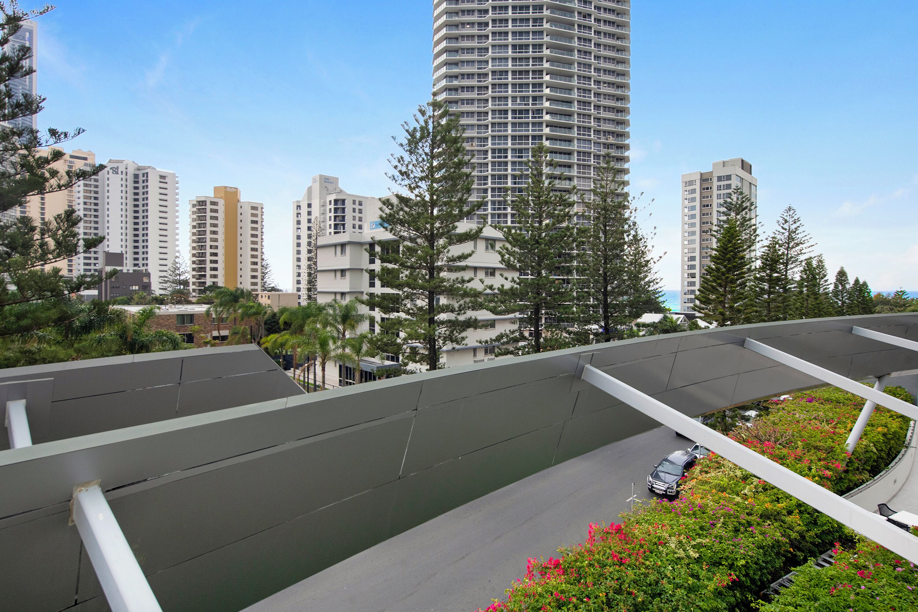 Paisagem urbana moderna com edifícios altos, uma ponte pedonal curva e um carro na estrada.
