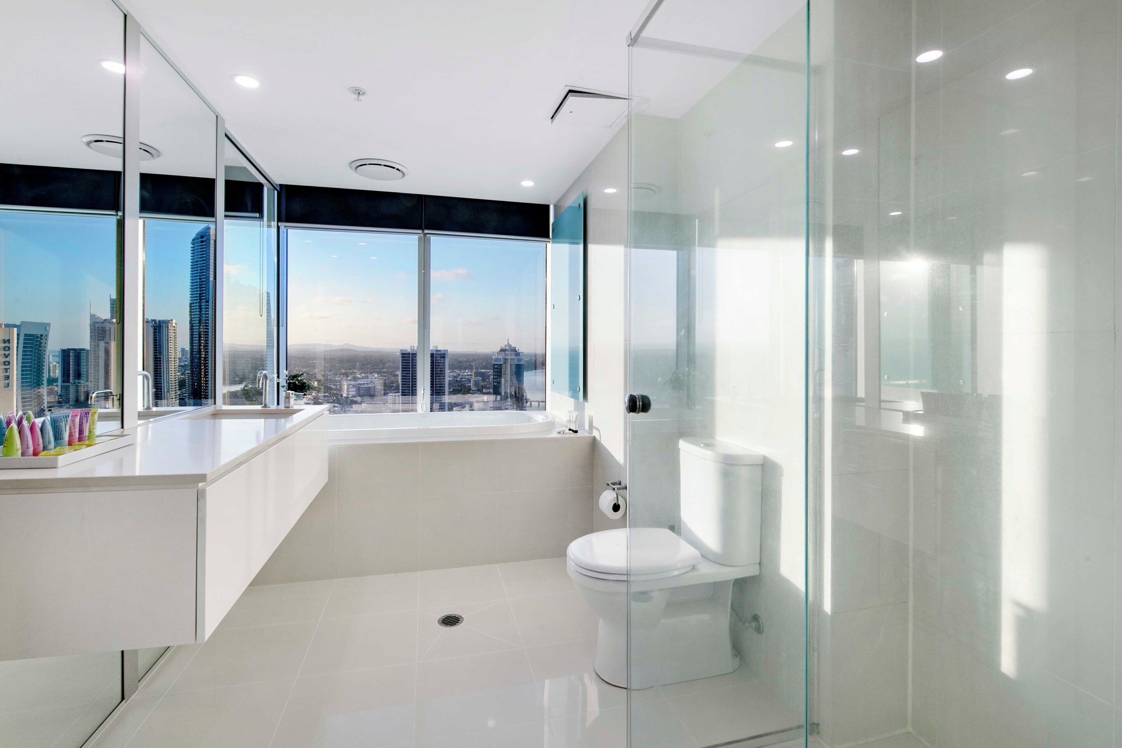 A modern bathroom with a glass-enclosed shower, a toilet, and a large window offering a city view.