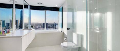 A modern bathroom with a glass-enclosed shower, a toilet, and a large window offering a city view.