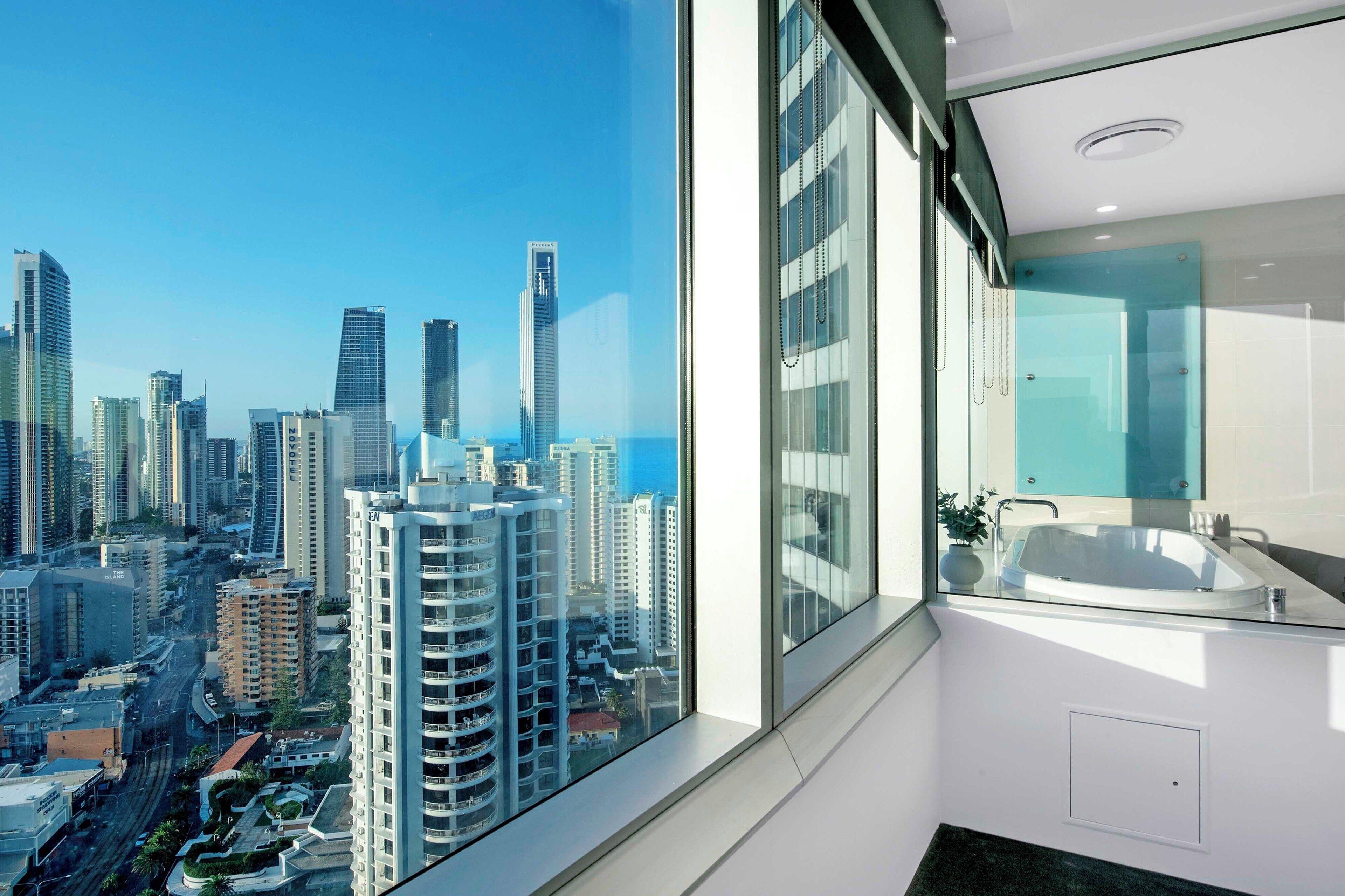 A modern bathroom with a large window, a glass-enclosed shower, and a view of a cityscape.