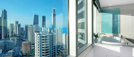 A modern bathroom with a large window, a glass-enclosed shower, and a view of a cityscape.