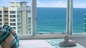 A hotel room with a large window offering a view of the ocean and a high-rise building. - Private Q Tower Apartments - WOWSTAY (Surfers Paradise)