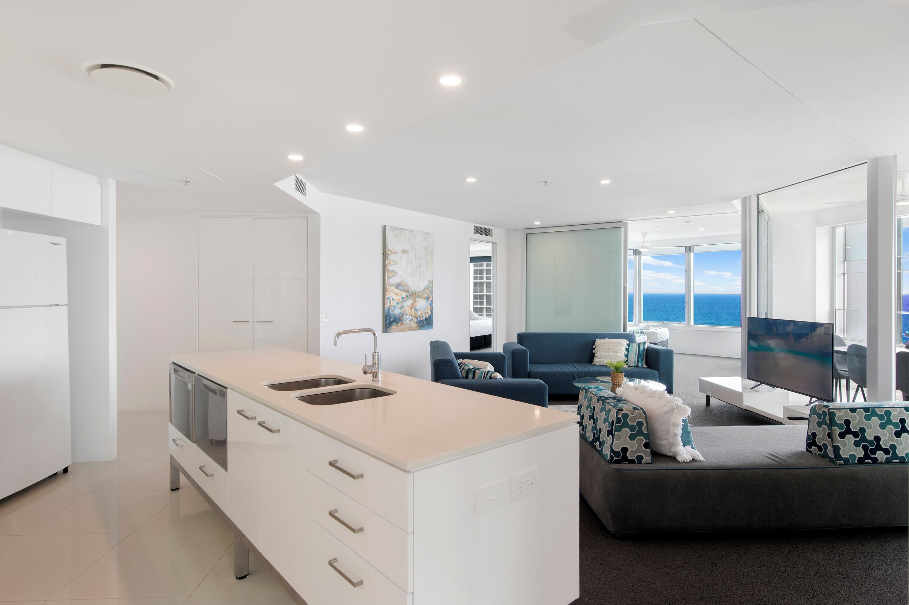 Una cocina moderna con una isla grande, un área de comedor con televisor y un sofá con vistas.
