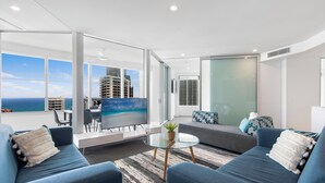 A modern living room with a large TV, seating area, and a view of the ocean. - Private Q Tower Apartments - WOWSTAY (Surfers Paradise)