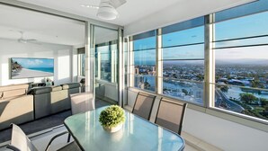 A modern room with a glass table, seating area, and a large window offering a city view. - Private Q Tower Apartments - WOWSTAY (Surfers Paradise)