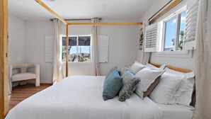 Un dormitorio con una cama grande, una silla, una ventana con persianas y vistas al exterior.
