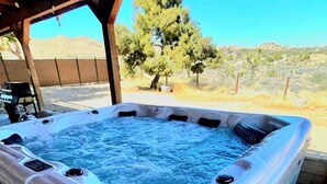 Un jacuzzi bajo una pérgola de madera con vistas despejadas a árboles y un paisaje desértico.