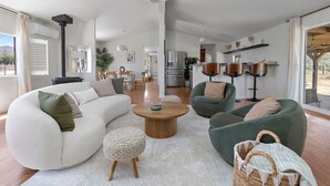 Una sala de estar moderna con un sofá blanco, sillones verdes, una mesa de centro y un comedor al fondo.