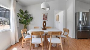 Una cocina moderna con refrigerador de acero inoxidable, mesa de comedor de madera con sillas y una planta en maceta.