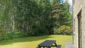 A picnic table in a grassy area with a stone building in the background. - Birch View -  Retreat Group (Aviemore)
