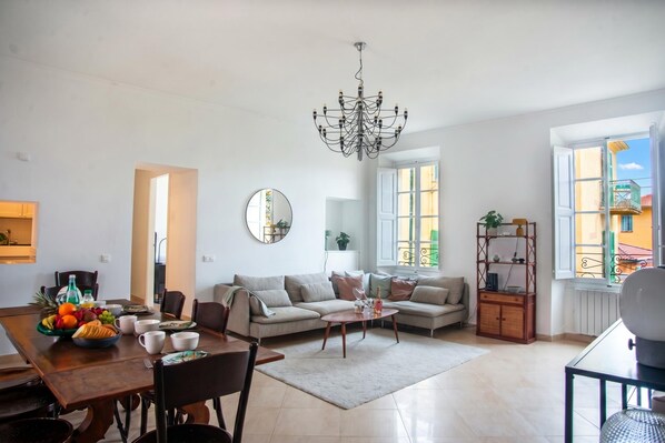 A spacious living room with a dining area, a chandelier, a sofa, a coffee table, and a view through large windows. - Saint Michel - Apartment in Old Town, Menton, France (Menton)