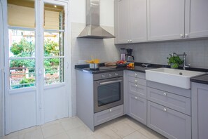 A modern kitchen with grey cabinets, a stainless steel oven, a sink, and a window overlooking a garden.
