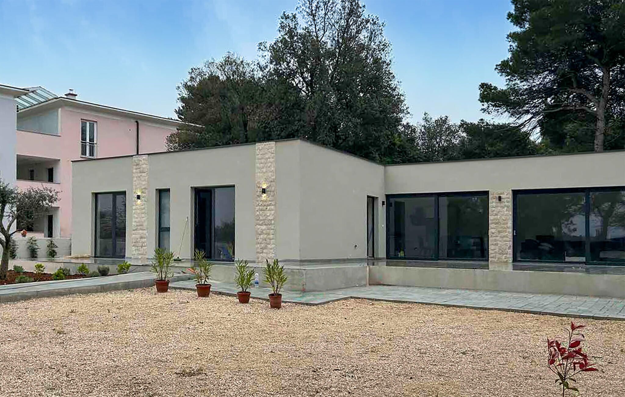A modern building with a flat roof, large windows, and a gravel courtyard with potted plants.
