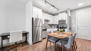 A modern kitchen with white cabinets, stainless steel appliances, and a wooden dining table with chairs.