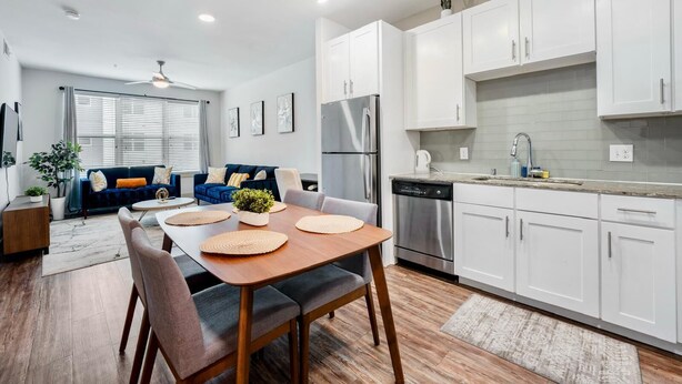 A modern kitchen with white cabinets, stainless steel appliances, and a dining area with a wooden table and chairs.