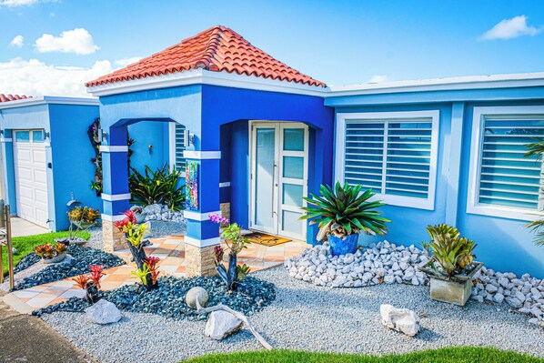 A blue house with a red roof, white shutters, and a well-maintained garden with various plants and rocks. - Blue Paradise in Fajardo, PR - - Beaches, Adventures, El Yunque (Fajardo)