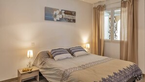 Ein Schlafzimmer mit einem Bett, zwei Nachttischen, einem Wandbild und einem Fenster mit Vorhängen.