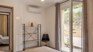 Une chambre comprenant un lit, une chaise, une étagère et une grande porte-fenêtre coulissante donnant sur un espace extérieur.
