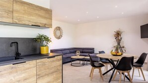 Une cuisine moderne avec des meubles en bois, un plan de travail noir et un évier. On y trouve également un coin repas avec une table ronde, des chaises noires et une plante en pot.