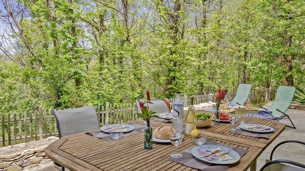 Un espace de restauration en plein air avec une table en bois dressée pour un repas, entourée de chaises et d’une clôture en bois.