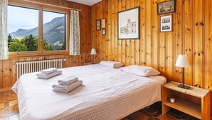 Ein Zimmer mit Holzwandverkleidung, einem großen Bett, zwei Nachttischen und Blick auf Berge durch ein Fenster.