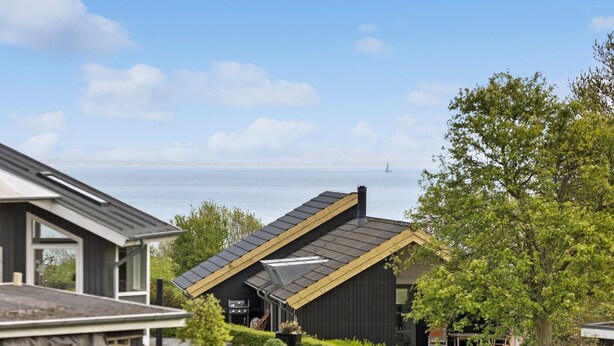 Une maison moderne avec un toit en pente, une cheminée bien visible et une vue sur la mer.